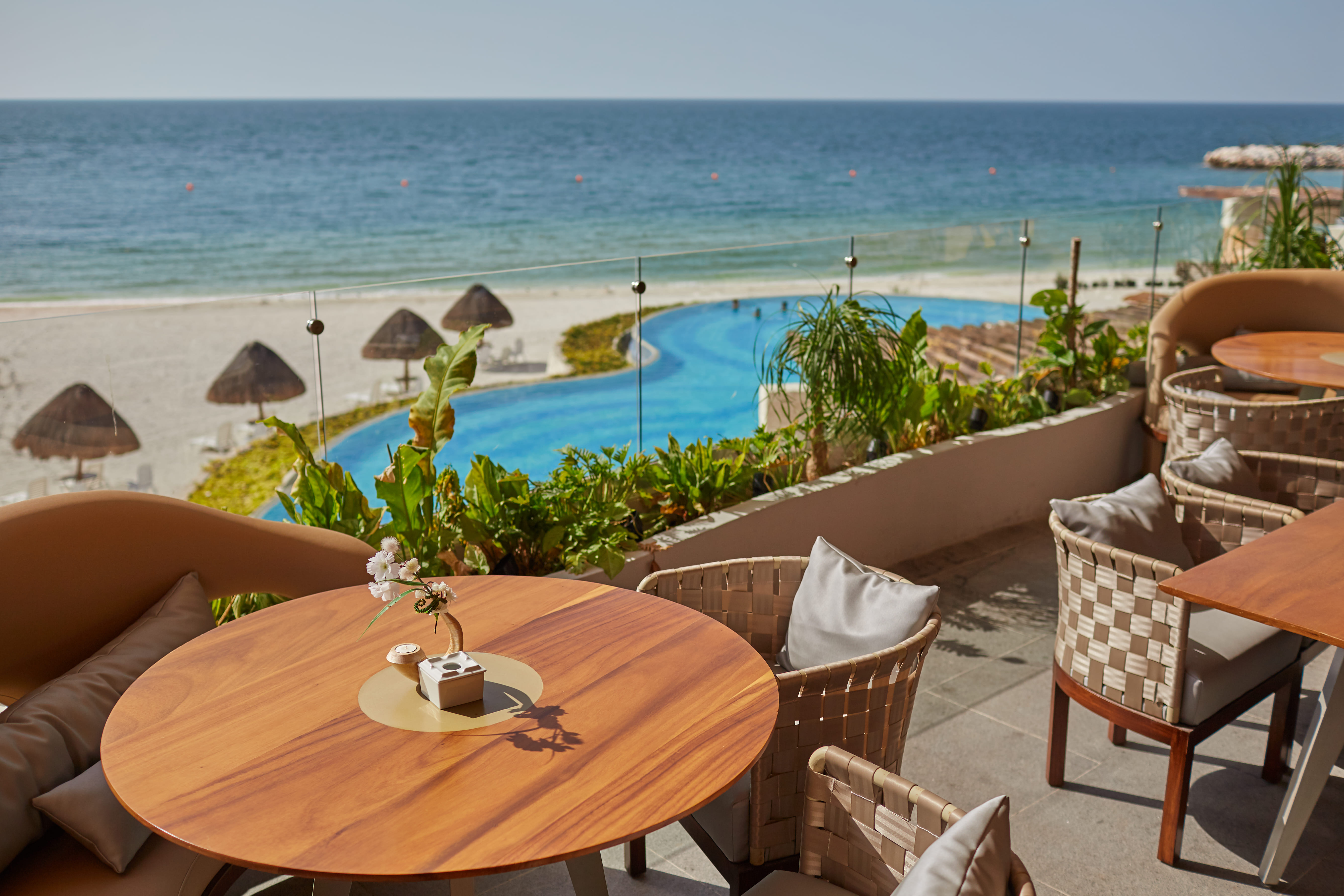 Beach club view with a pool and the ocean in the background, tables with chairs in the foreground